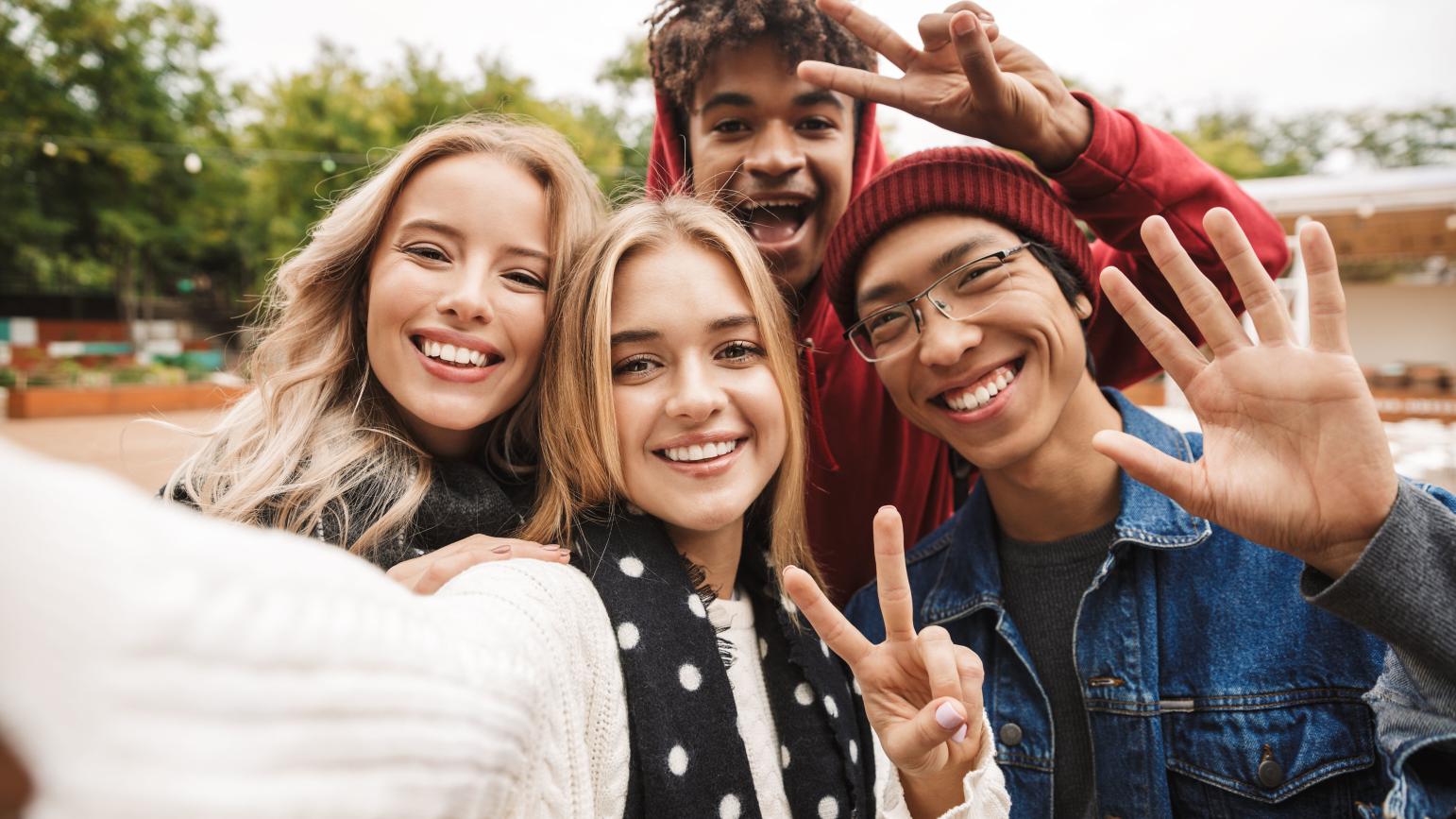 Vier junge Menschen winken in die Kamera