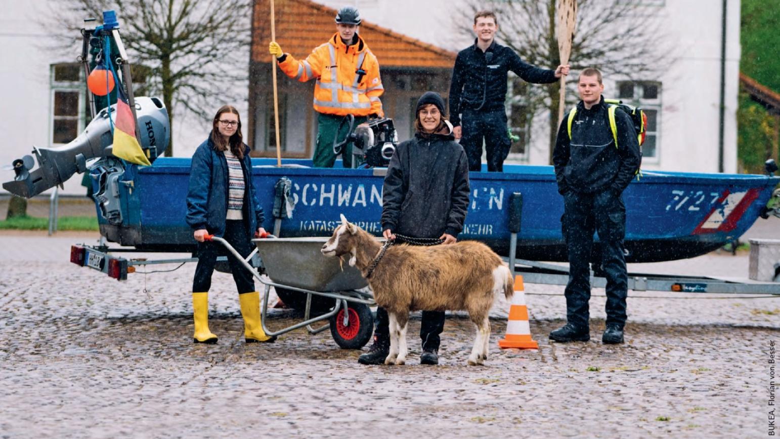 Fünf Jungerwachsene mit einer Ziege und einem Boot des Katastrophenschutzes