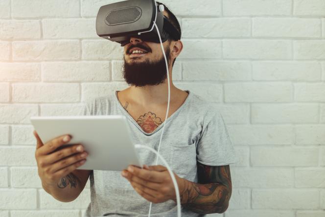 ein junger Mann hält ein Tablet in der Hand und trägt eine VR-Brille.