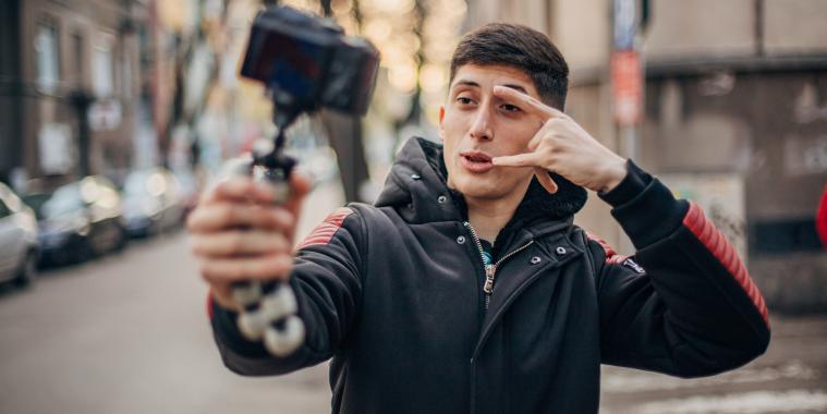 ein junger Mann hält einen Selfiestick in der Hand und filmt sich selbst.